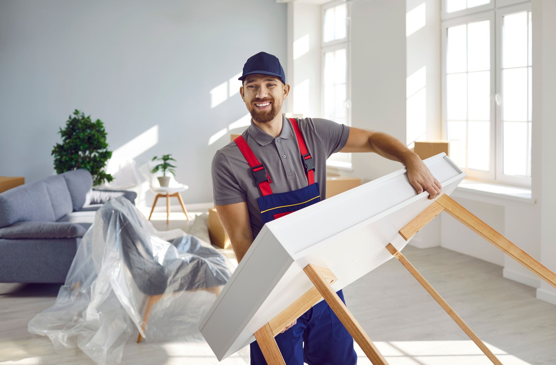 Happy young truck delivery or moving company worker carrying furniture and smiling